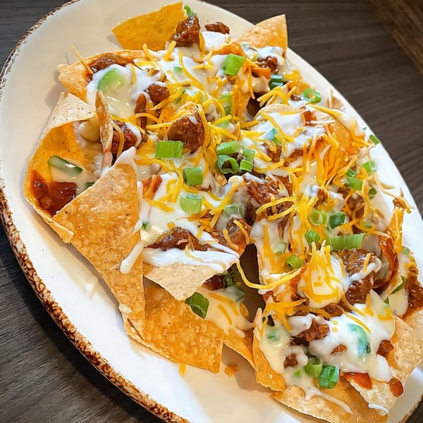 Loaded nachos with ground beef, melted cheese, sour cream, and green onions on a white plate.