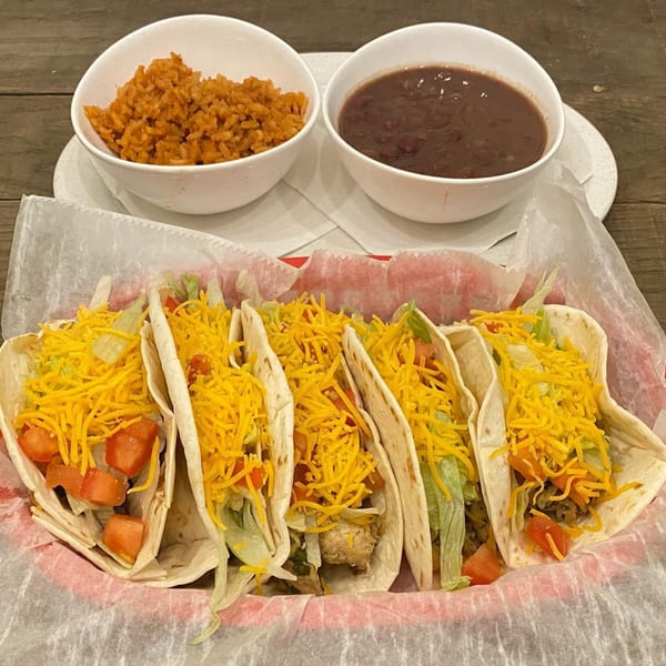 Five soft tacos with shredded cheese, lettuce, and tomatoes, served with rice and beans.