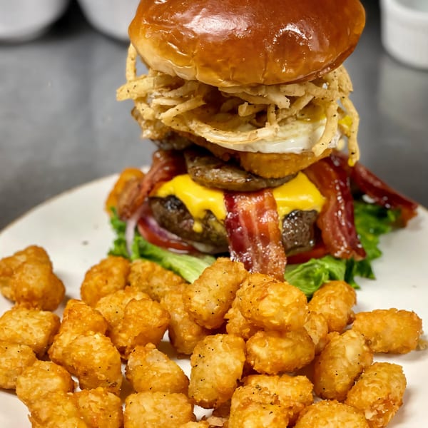 A towering Texas Forever burger with bacon, fried egg, onion strings, and tater tots.