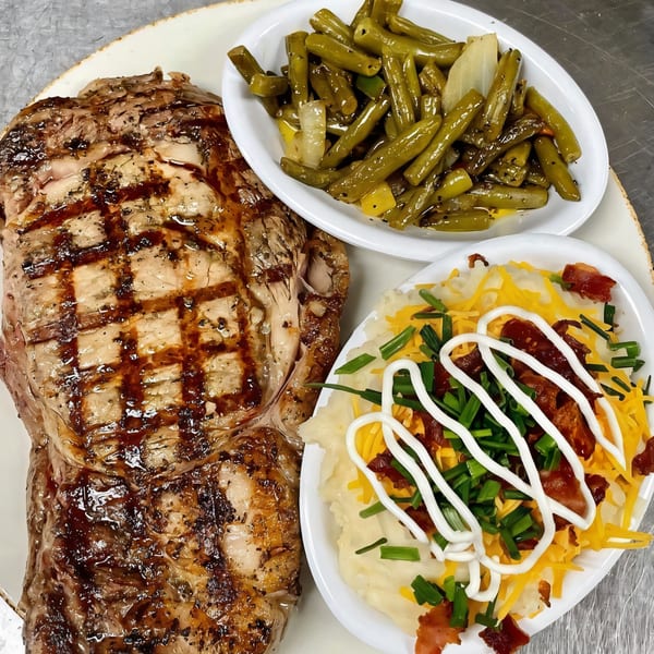Grilled steak with green beans and loaded mashed potatoes, topped with cheese, bacon, and chives.