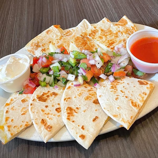 A plate of quesadilla wedges with a side of pico de gallo, sour cream, and salsa.
